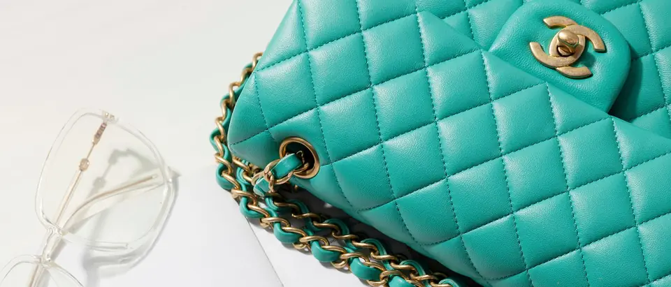 A teal quilted Chanel Classic Flap bag with gold chain on a white flat lay