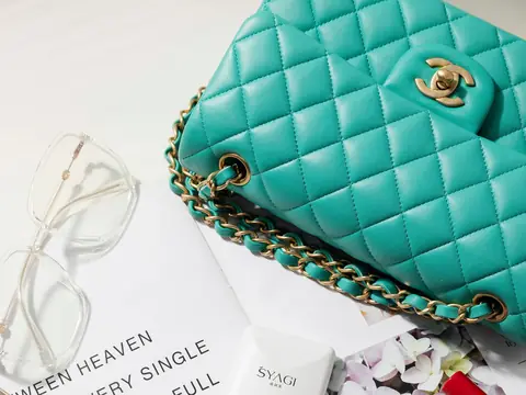 A teal quilted Chanel Classic Flap bag with gold chain on a white flat lay