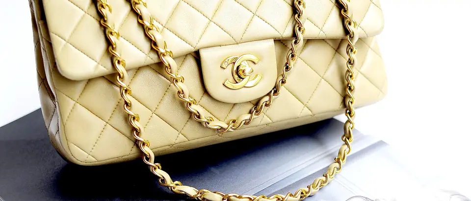 A cream quilted Chanel 2.55 flap bag with gold chain on a white background