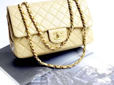 A cream quilted Chanel 2.55 flap bag with gold chain on a white background